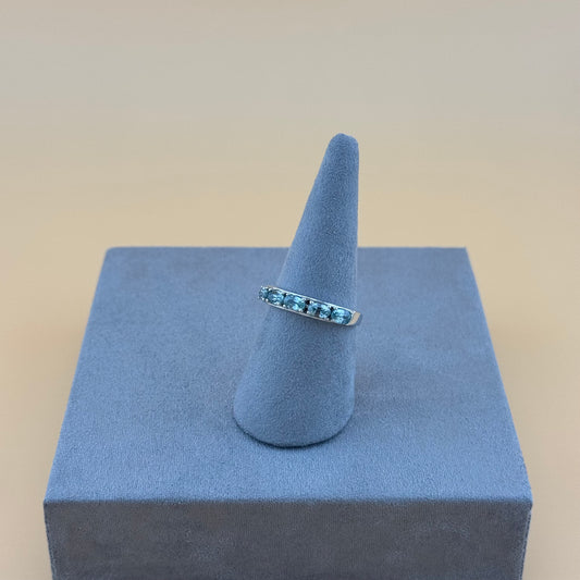 Silver ring with blue gemstones on a blue ring stand against a beige background