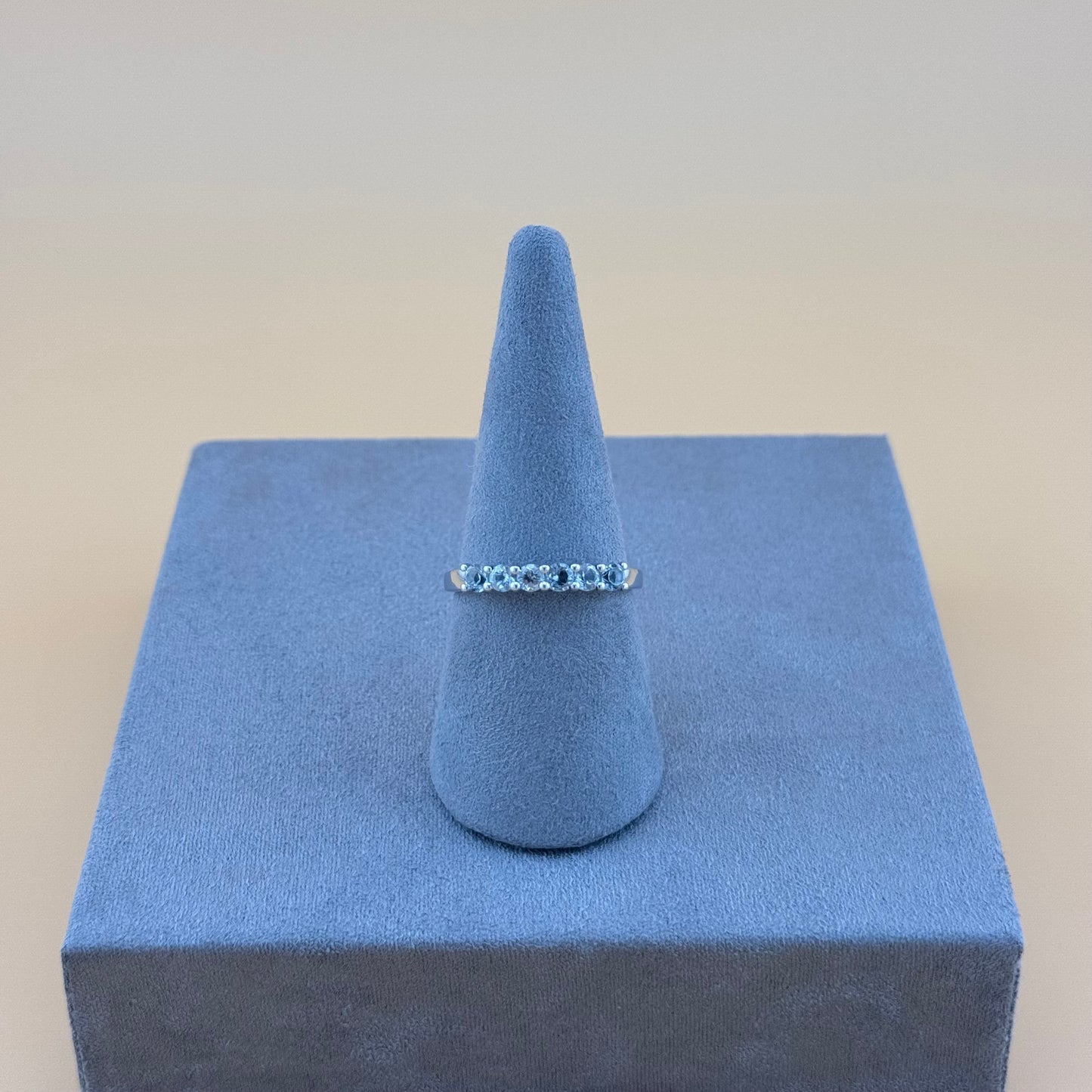 Silver aquamarine ring on a blue cone-shaped jewelry display against a beige background