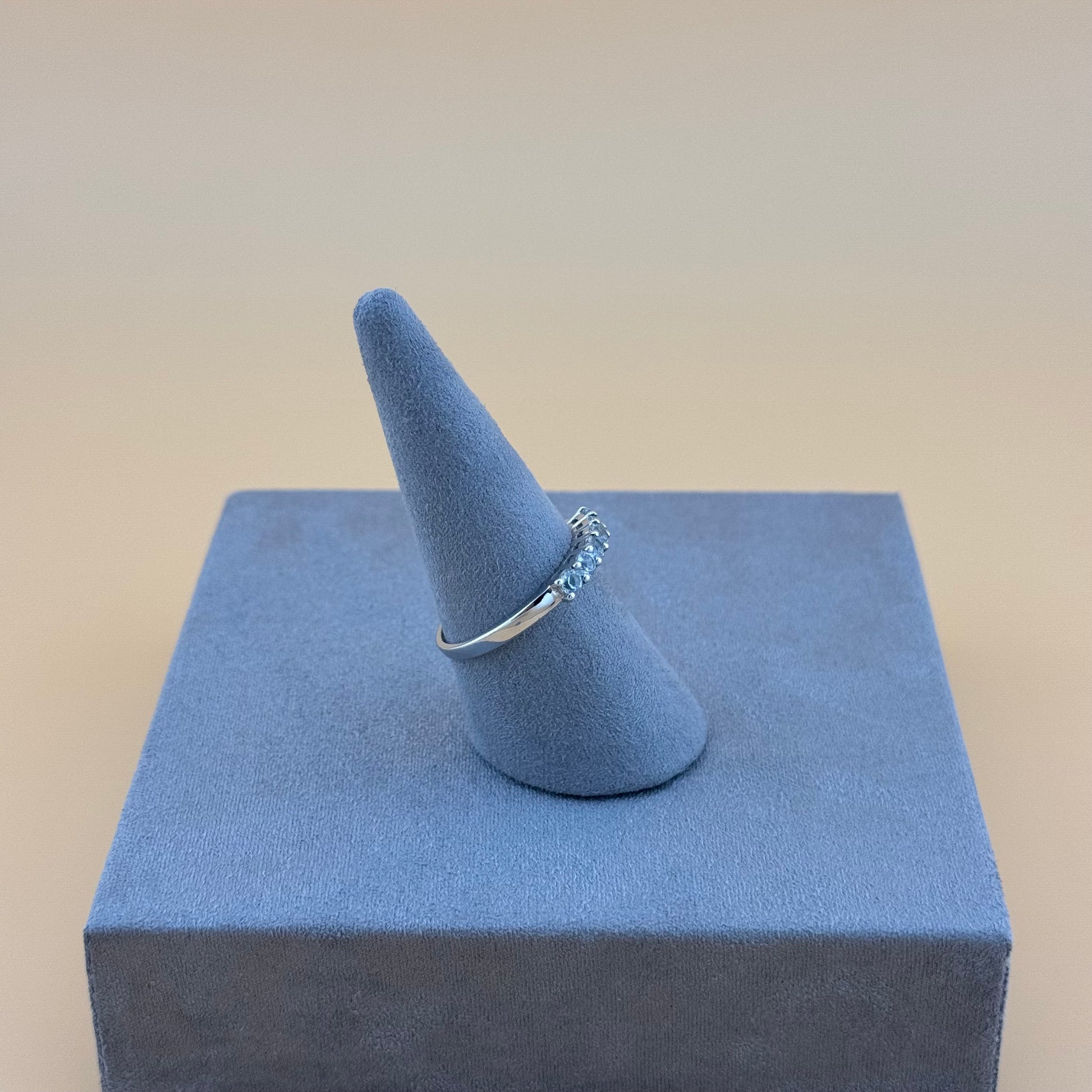 Silver ring on a blue cone-shaped jewelry display against a beige background