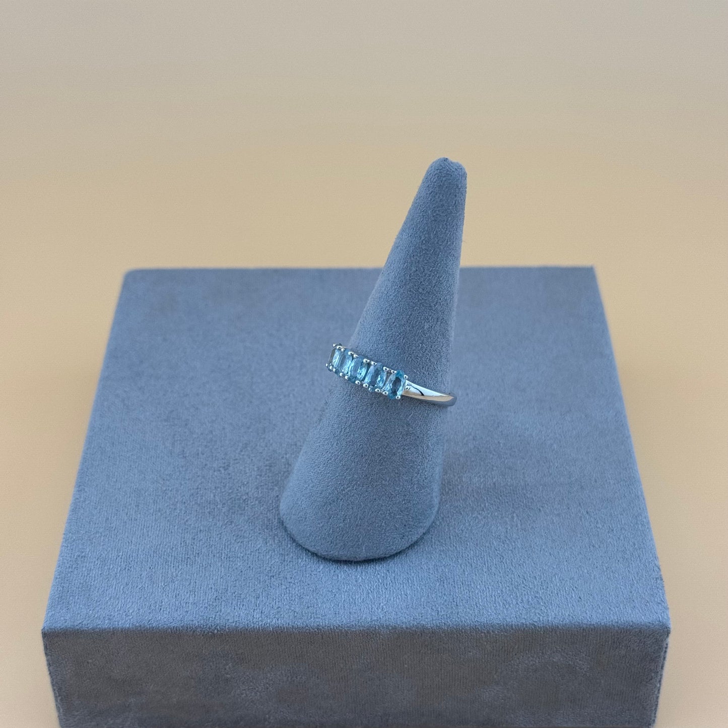 Silver ring with blue aquamarine gemstones on a gray cone-shaped stand against a beige background