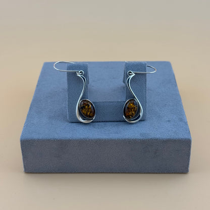 Pair of silver earrings with amber stones on a blue cushion against a beige background