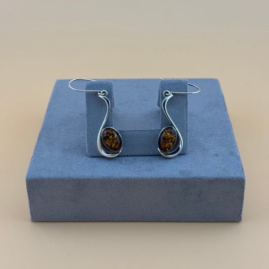 Pair of silver earrings with amber stones on a blue cushion against a beige background