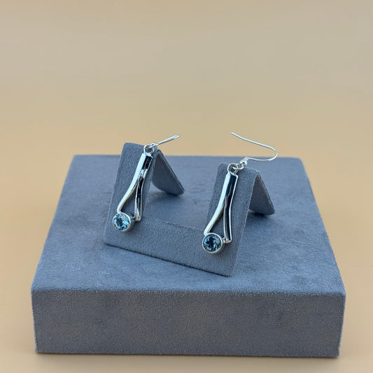 Silver earrings with blue aquamarine gemstones on a gray stand against a beige background