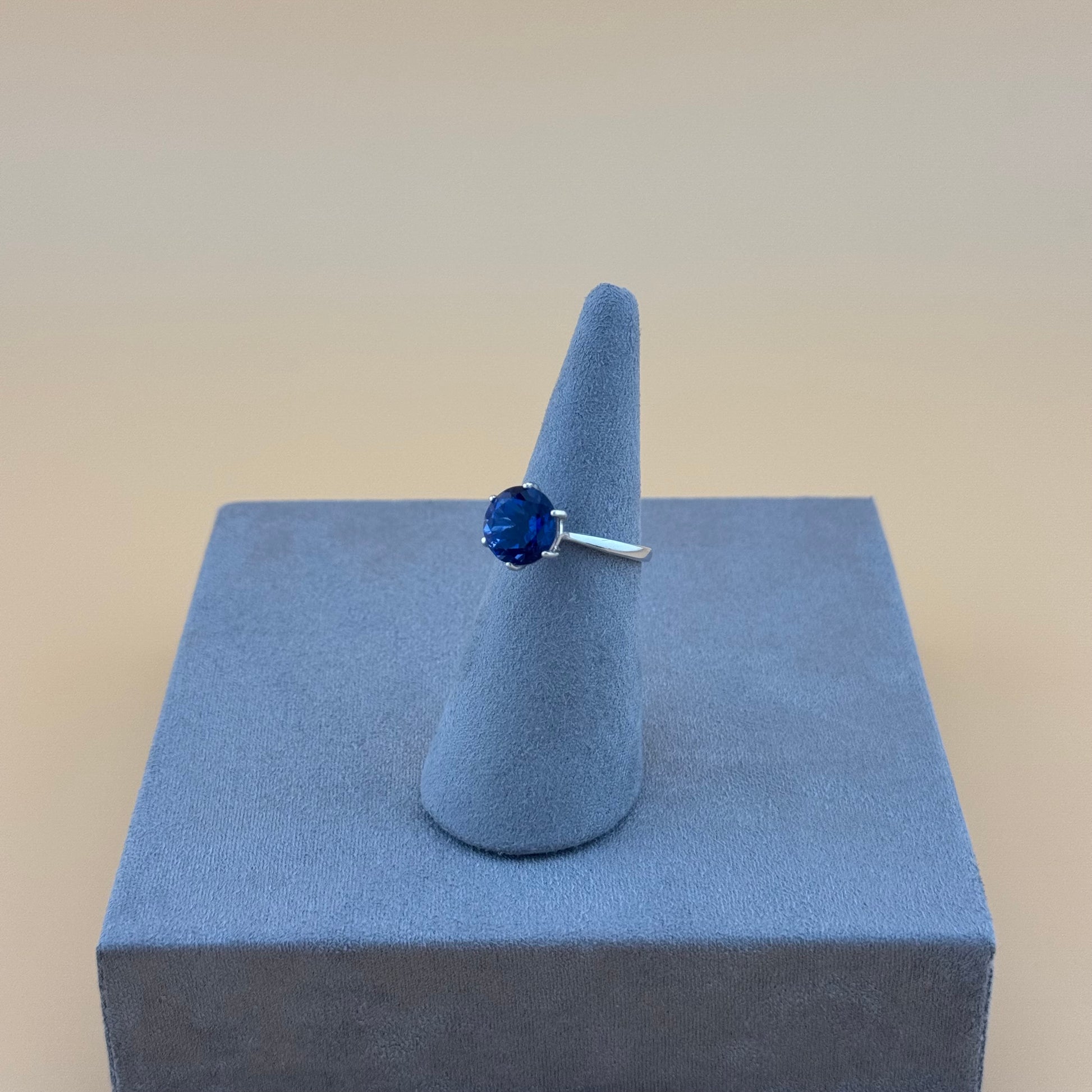 Blue sapphire gemstone ring on a gray cone-shaped stand against a beige background