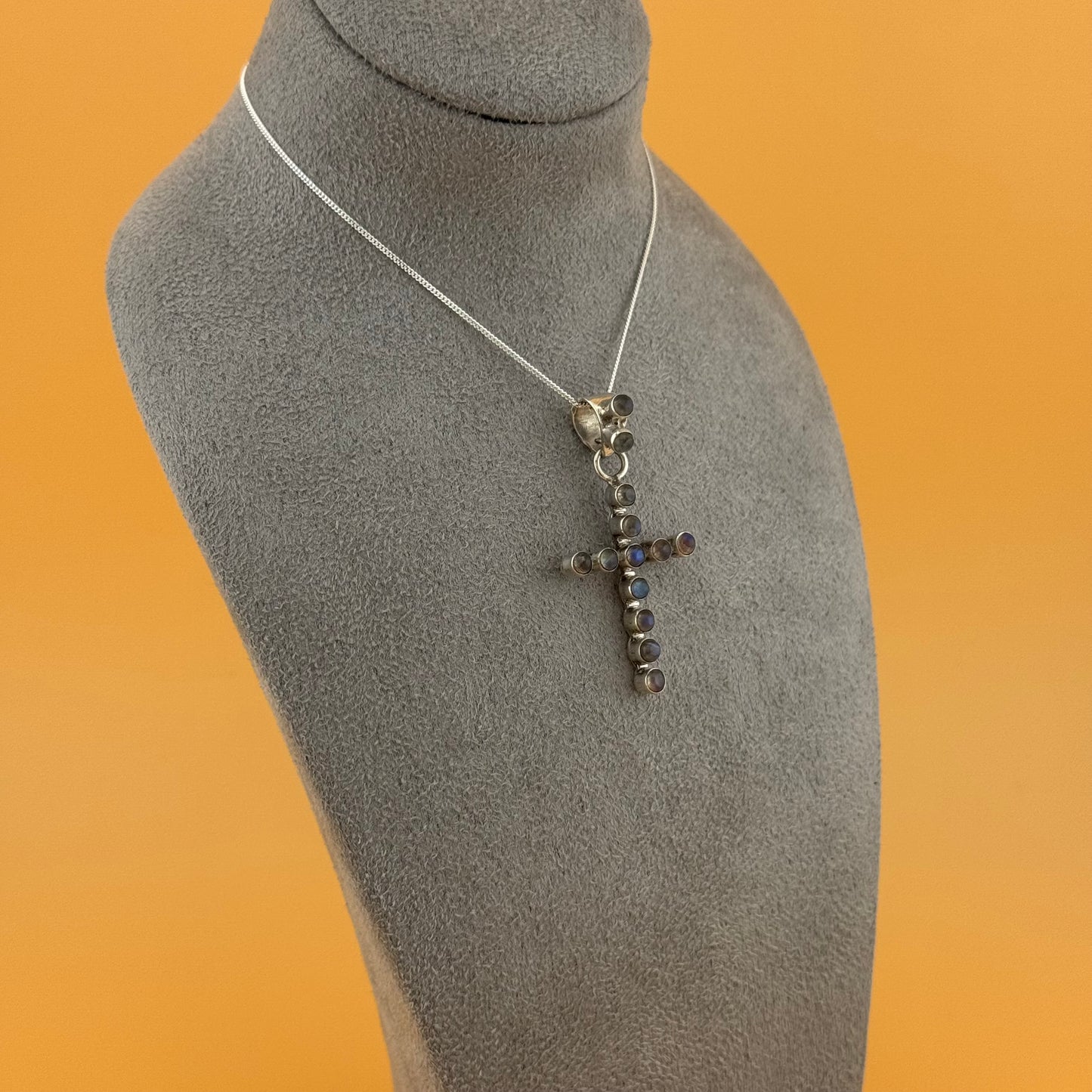 Silver labradorite cross pendant necklace on a gray mannequin bust against an orange background