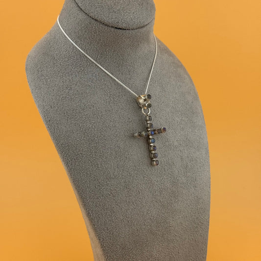 Silver labradorite cross pendant necklace on a gray mannequin bust against an orange background