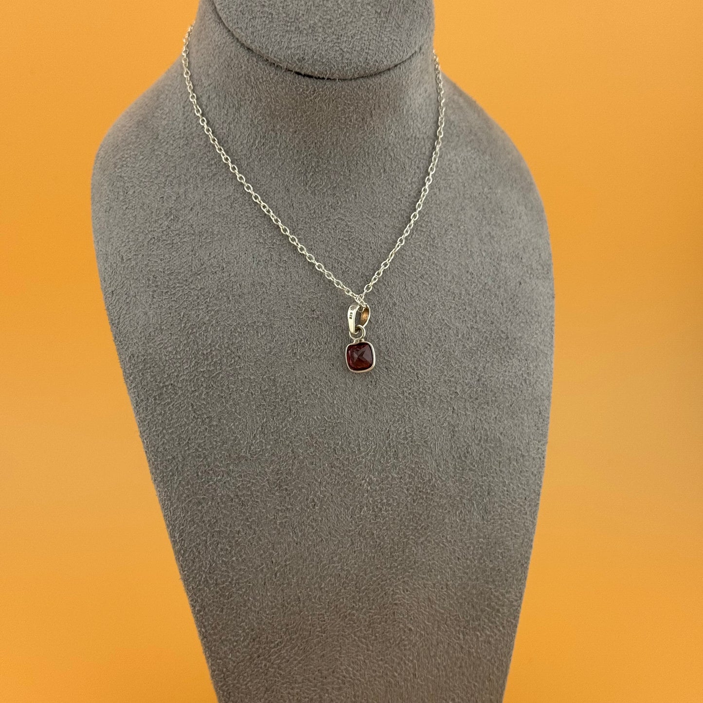 Silver necklace with a garnet pendant on a gray mannequin bust against an orange background