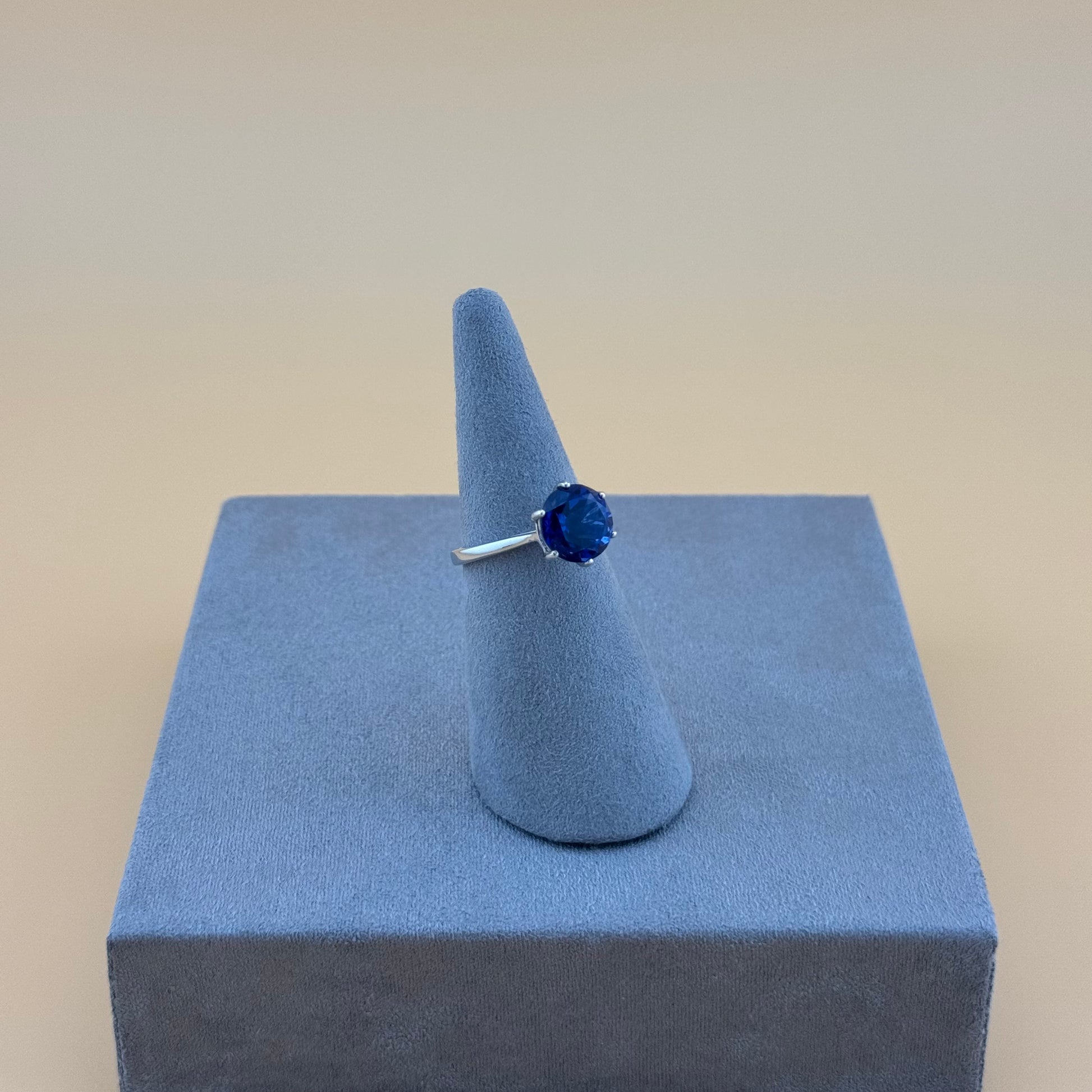 Ring with a blue sapphire gemstone on a gray stand against a beige background