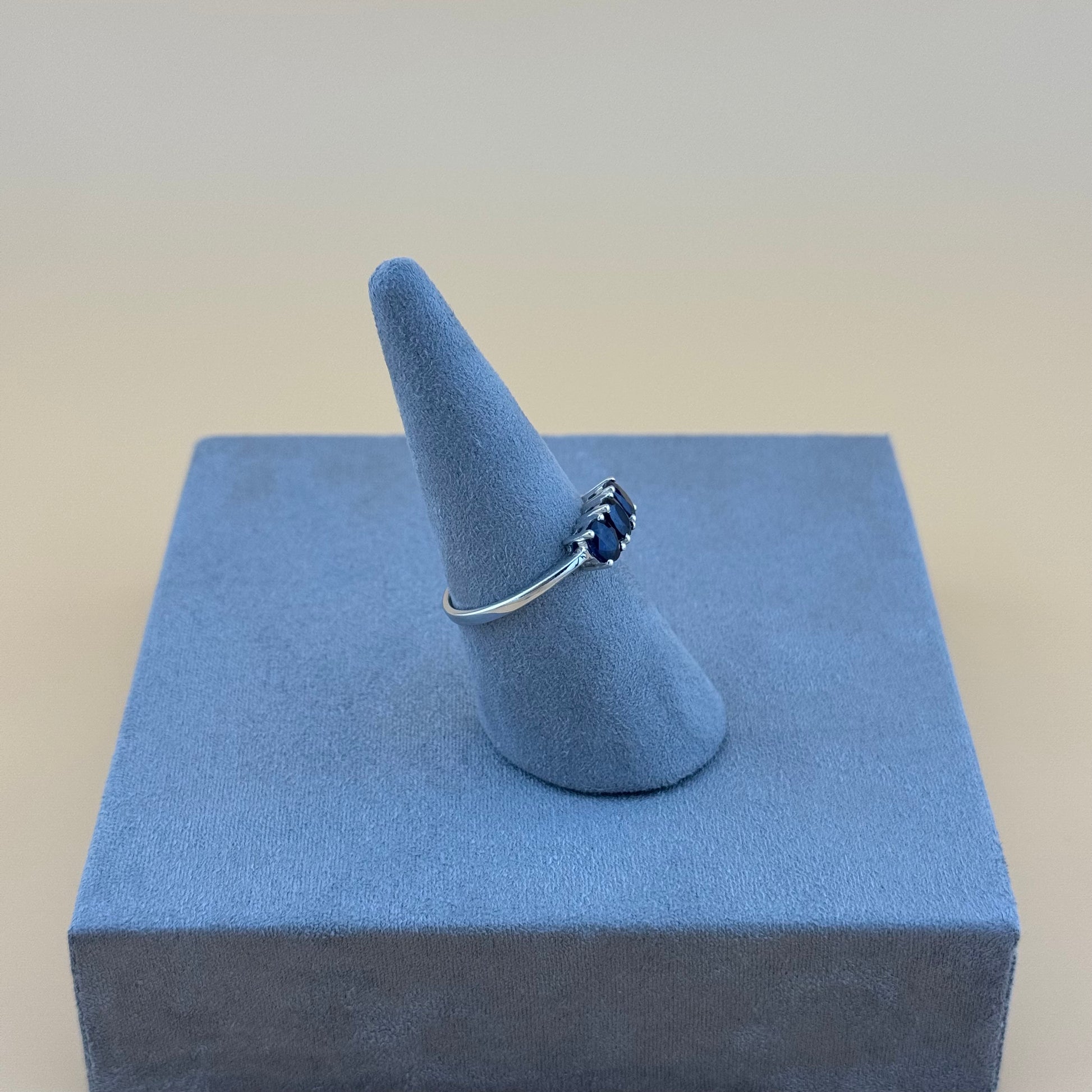 Silver ring with blue sapphire gemstone on a blue cone-shaped stand against a beige background