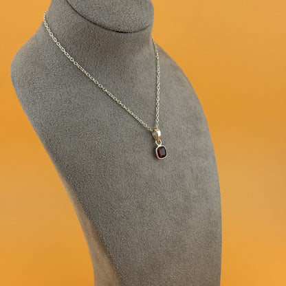 Necklace with a garnet pendant on a gray mannequin bust against an orange background