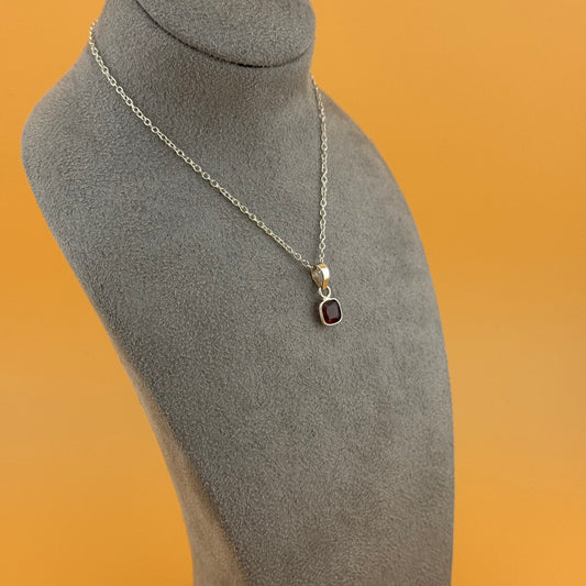 Necklace with a garnet pendant on a gray mannequin bust against an orange background