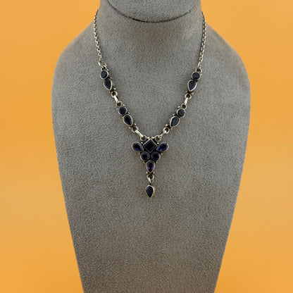 Necklace with purple iolite stones on a gray mannequin bust against an orange background