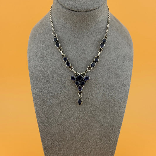Necklace with purple iolite stones on a gray mannequin bust against an orange background