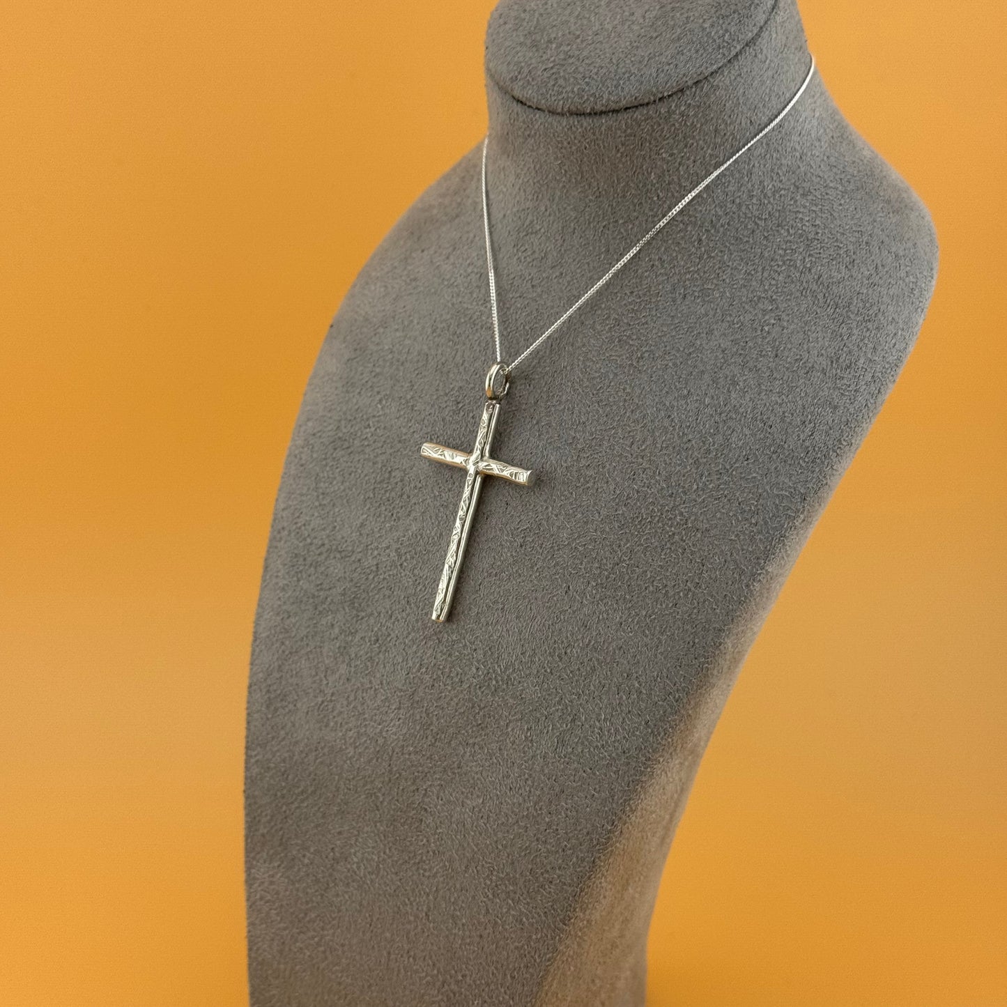 Silver cross necklace on a mannequin bust with an orange background