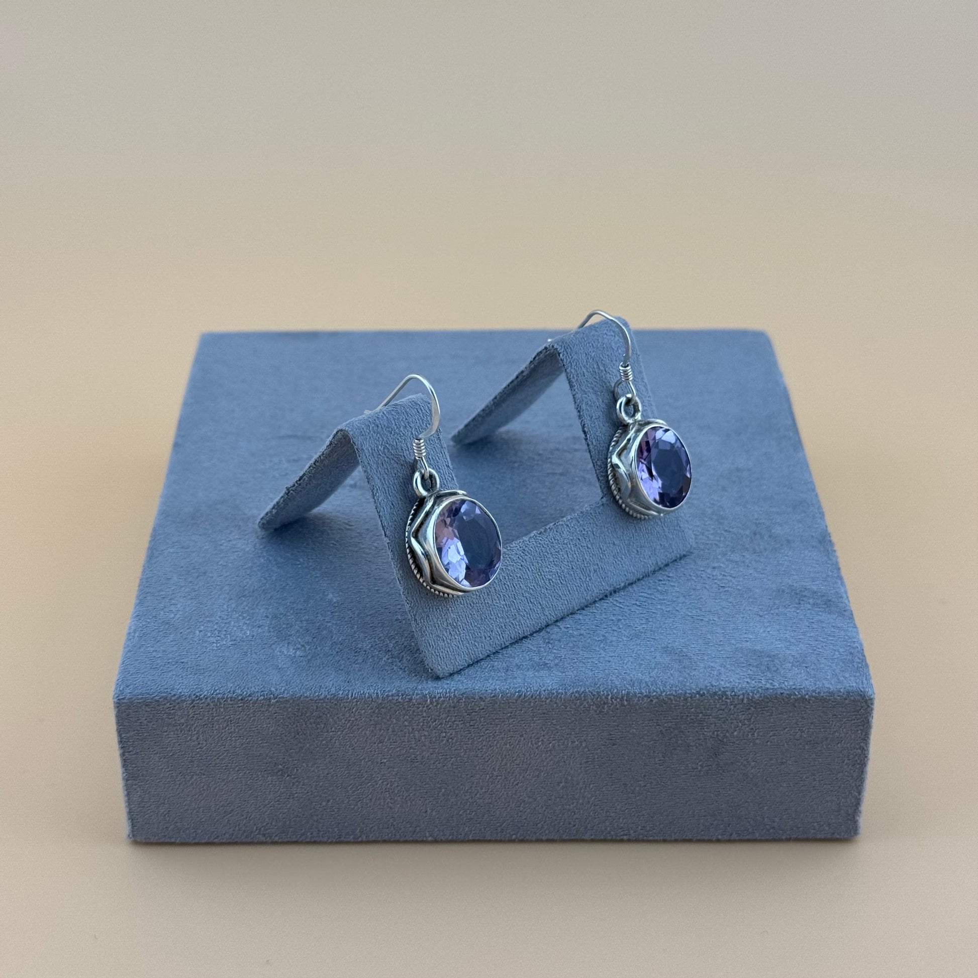 Pair of silver earrings with purple amethyst stones on a blue jewelry display block.
