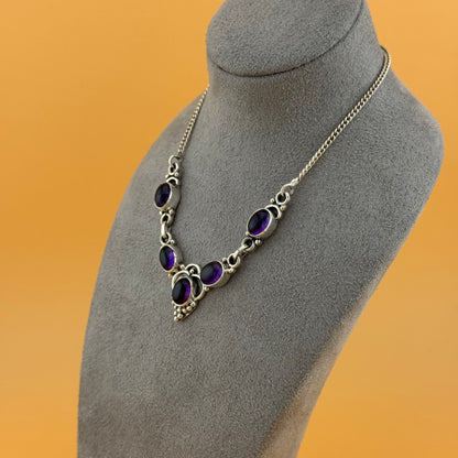 Necklace with purple amethyst stones on a gray mannequin bust against an orange background