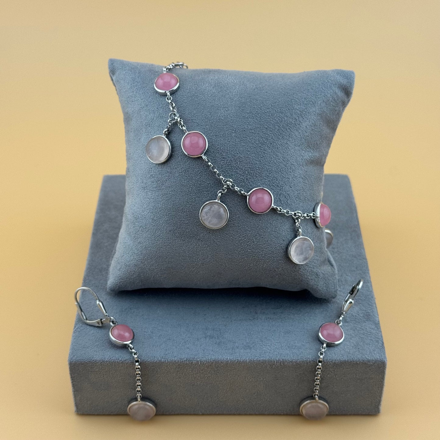 Bracelet with rose quartz pink and silver charms on a gray cushion against a beige background