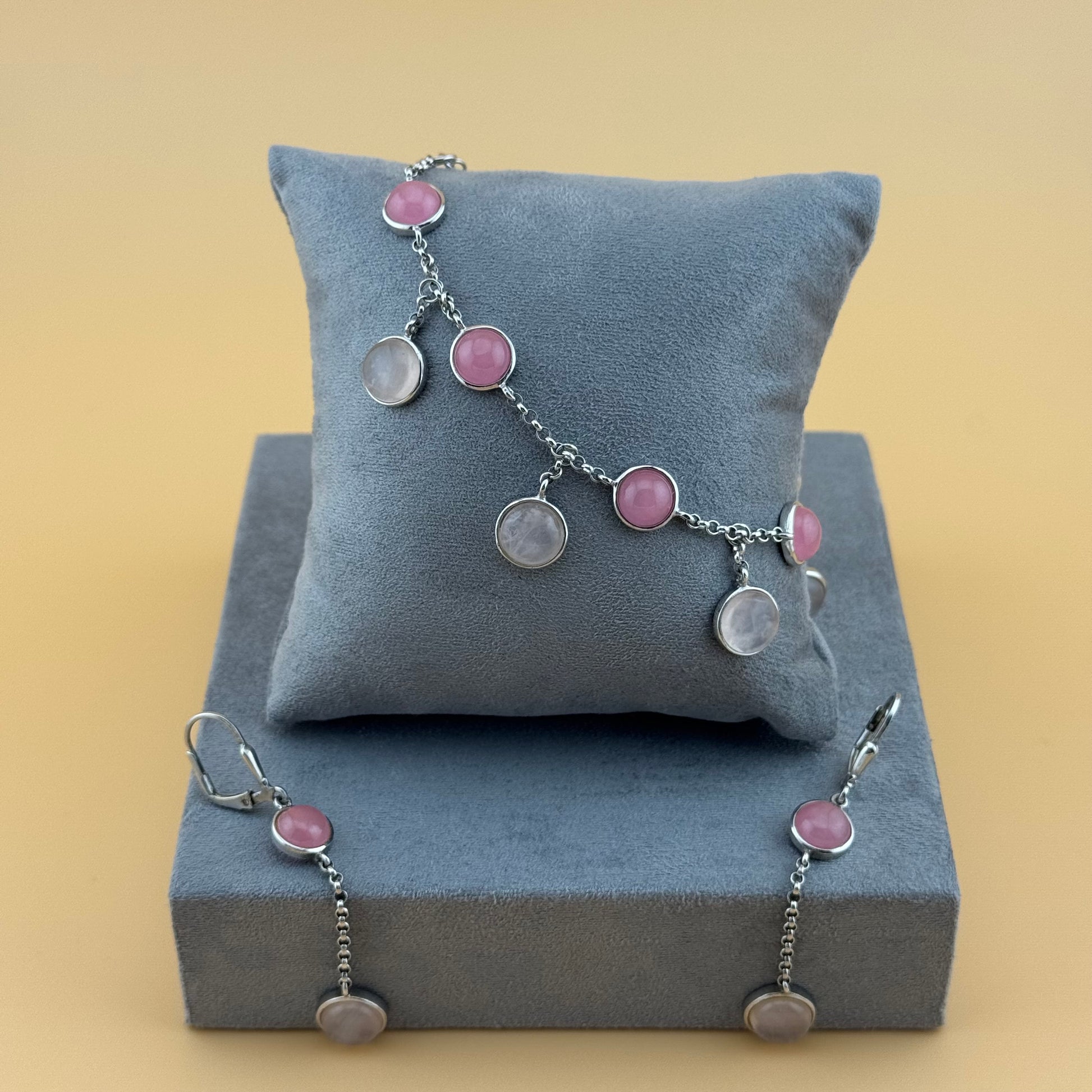 Bracelet with rose quartz pink and silver charms on a gray cushion against a beige background
