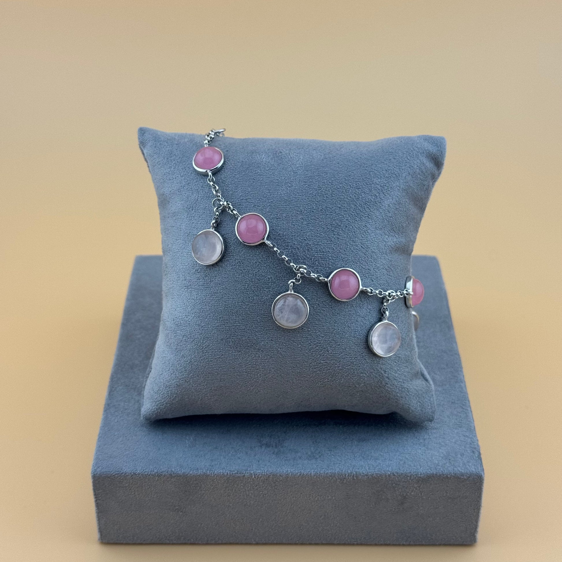 Bracelet with rose quartz pink and clear stones on a blue cushion against a beige background