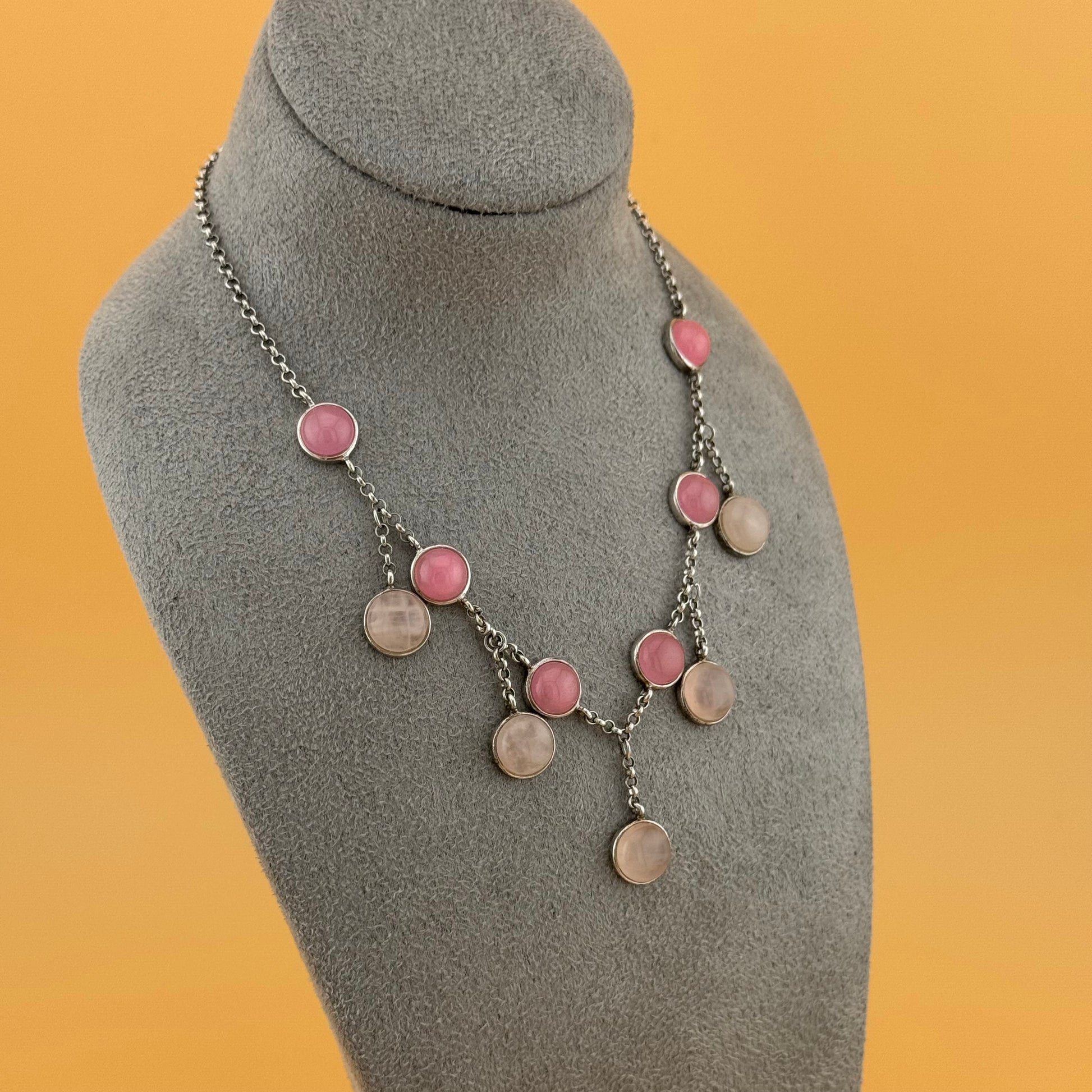 Necklace with pink and silver rose quartzcircular pendants on a gray mannequin bust against an orange background