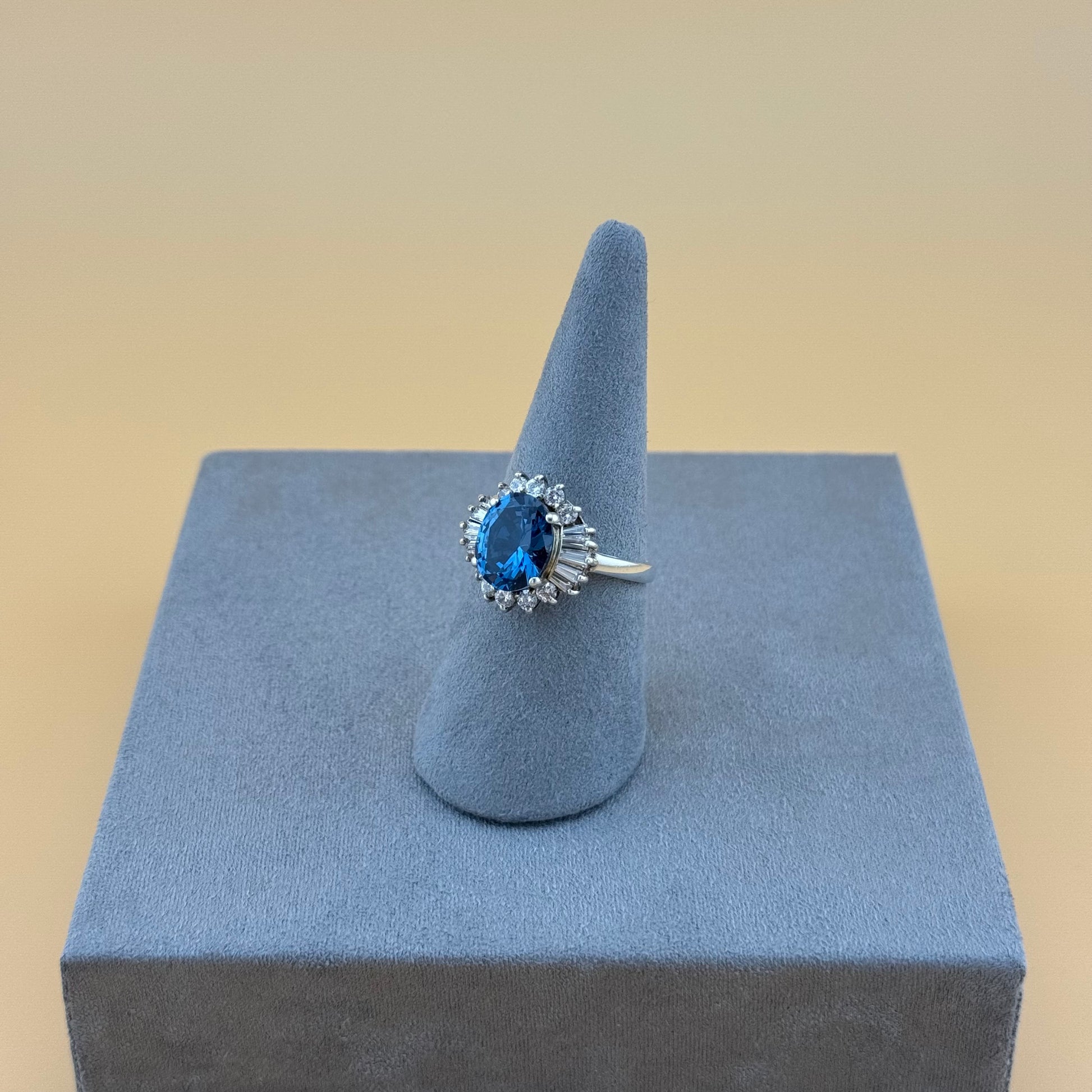 Silver ring with a London blue topaz gemstone on a gray stand against a beige background