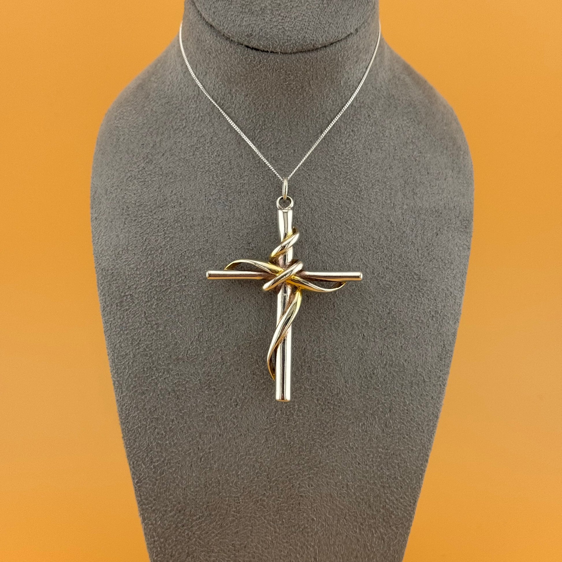 silver cross pendant on a gray mannequin bust with an orange background