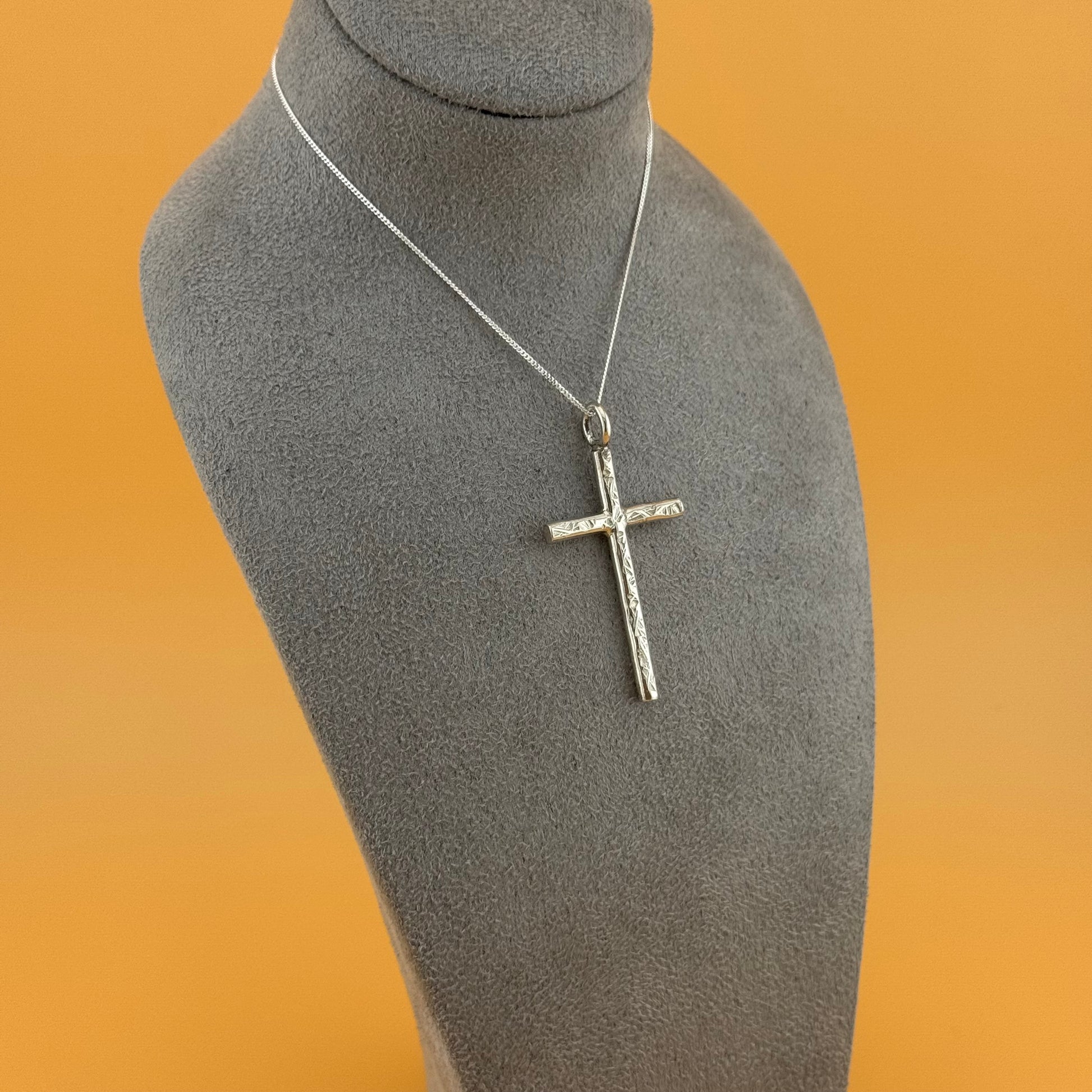 Silver cross pendant on a mannequin bust with an orange background