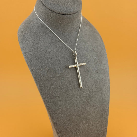 Silver cross pendant on a mannequin bust with an orange background
