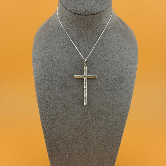 Silver cross pendant on a gray mannequin bust with an orange background