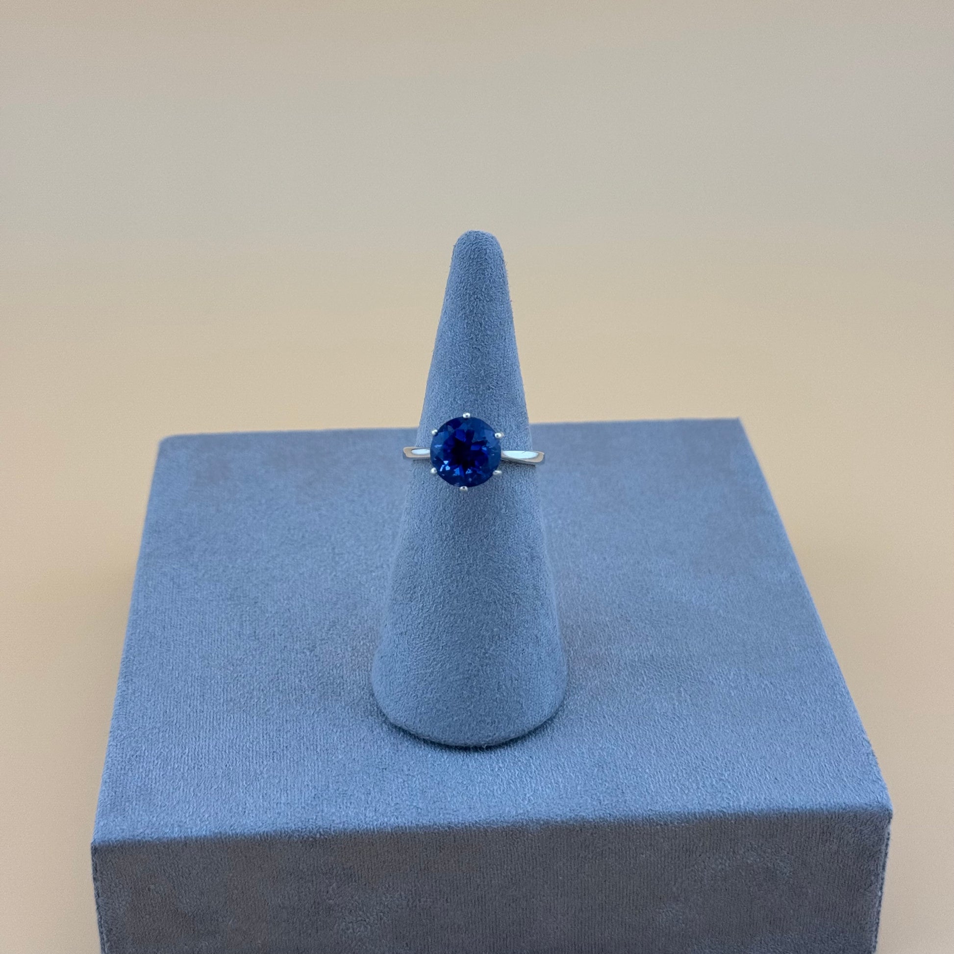 Ring with a blue gemstone on a gray cone and square stand against a beige background