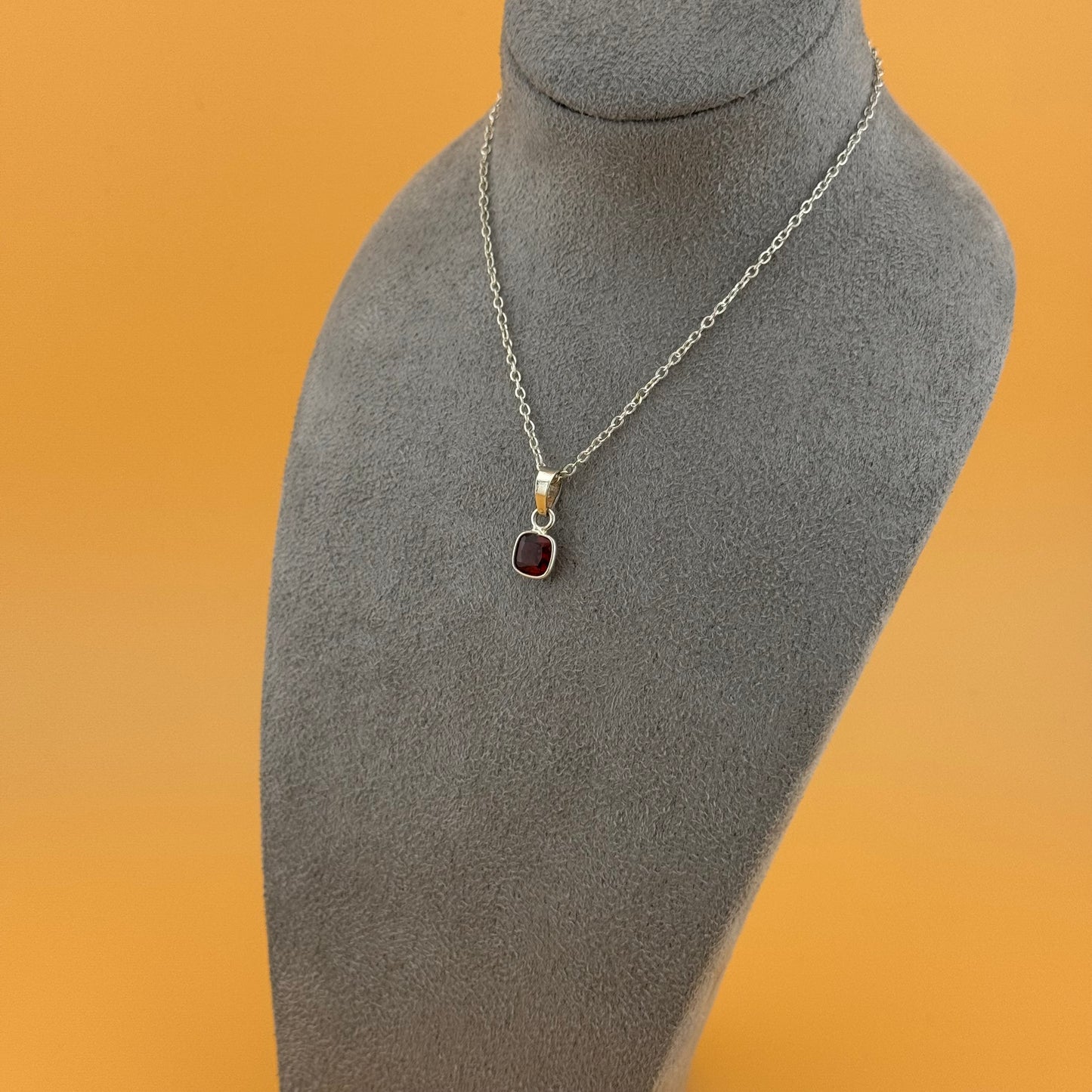 Necklace with a garnet pendant on a mannequin bust against an orange background