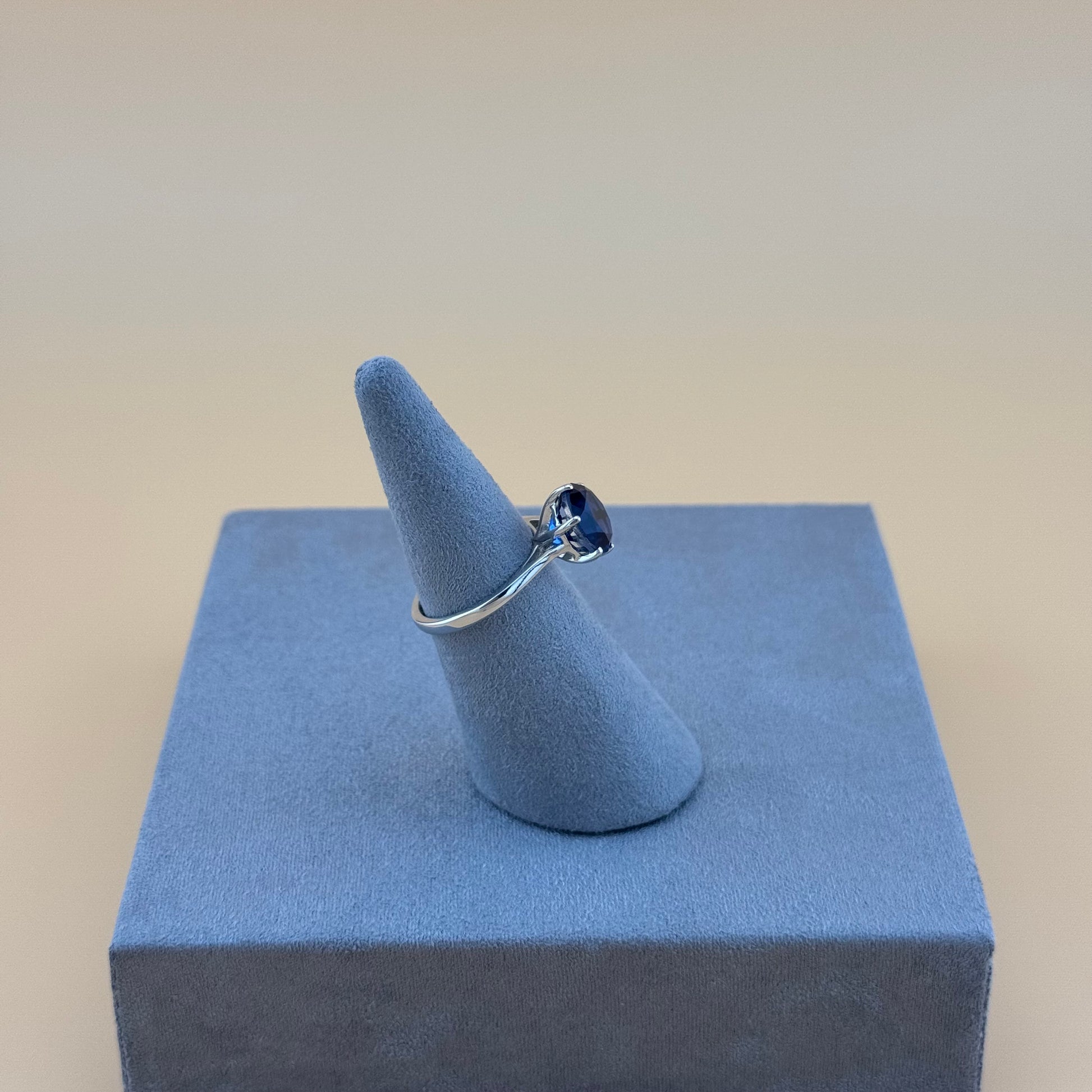 Silver ring with a blue gemstone on a blue ring cushion against a beige background