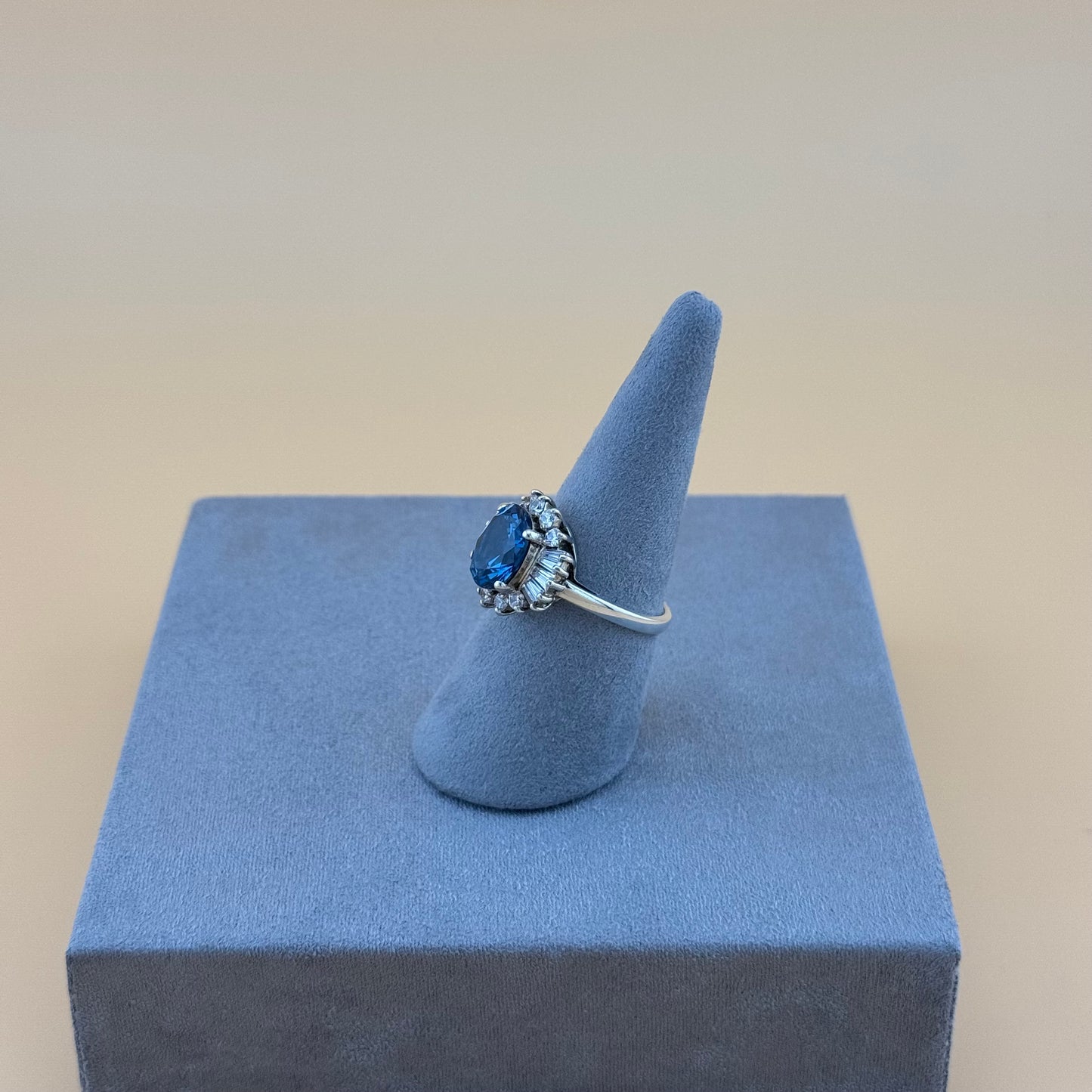 Ring with a blue gemstone on a blue stand against a beige background