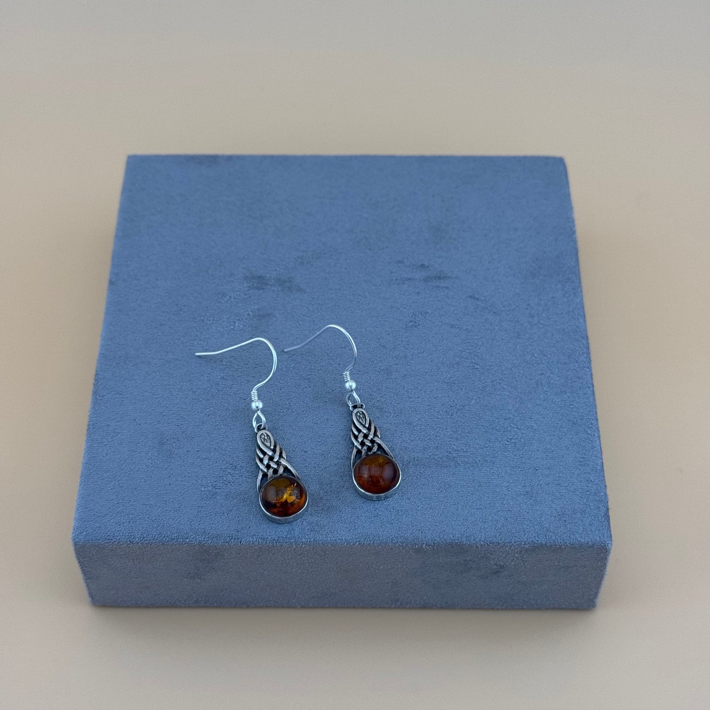 Pair of silver amber earrings with amber stones on a blue jewelry box.