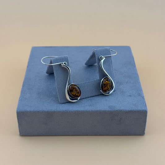 Silver earrings with amber stones on a blue cushion against a beige background