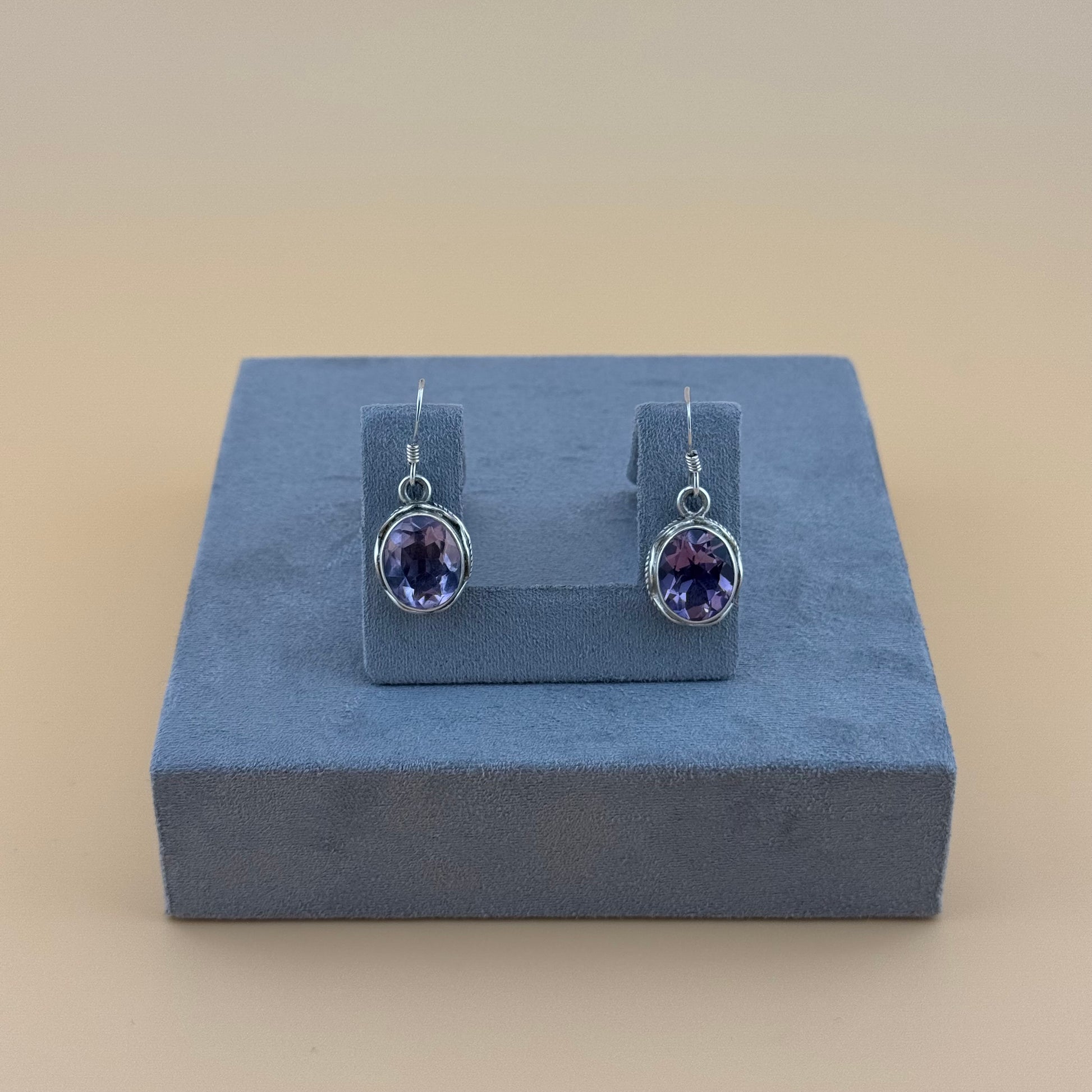 Pair of purple amethyst gemstone earrings on a blue stand against a beige background