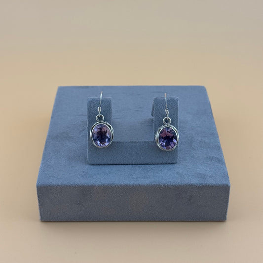 Pair of purple amethyst gemstone earrings on a blue stand against a beige background
