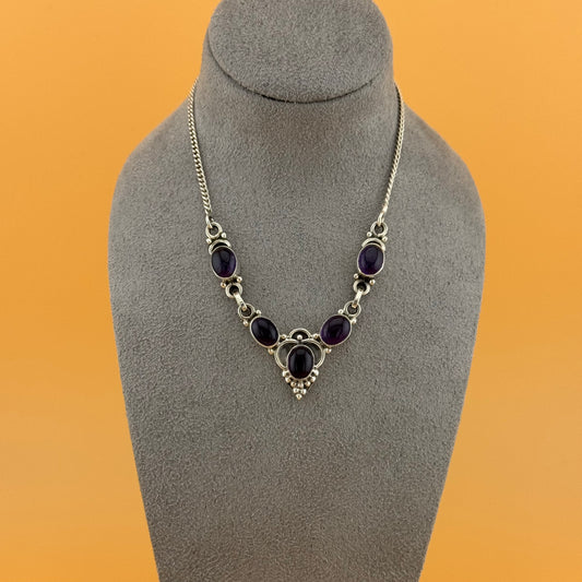 Necklace with purple amethyst stones on a gray mannequin bust against an orange background