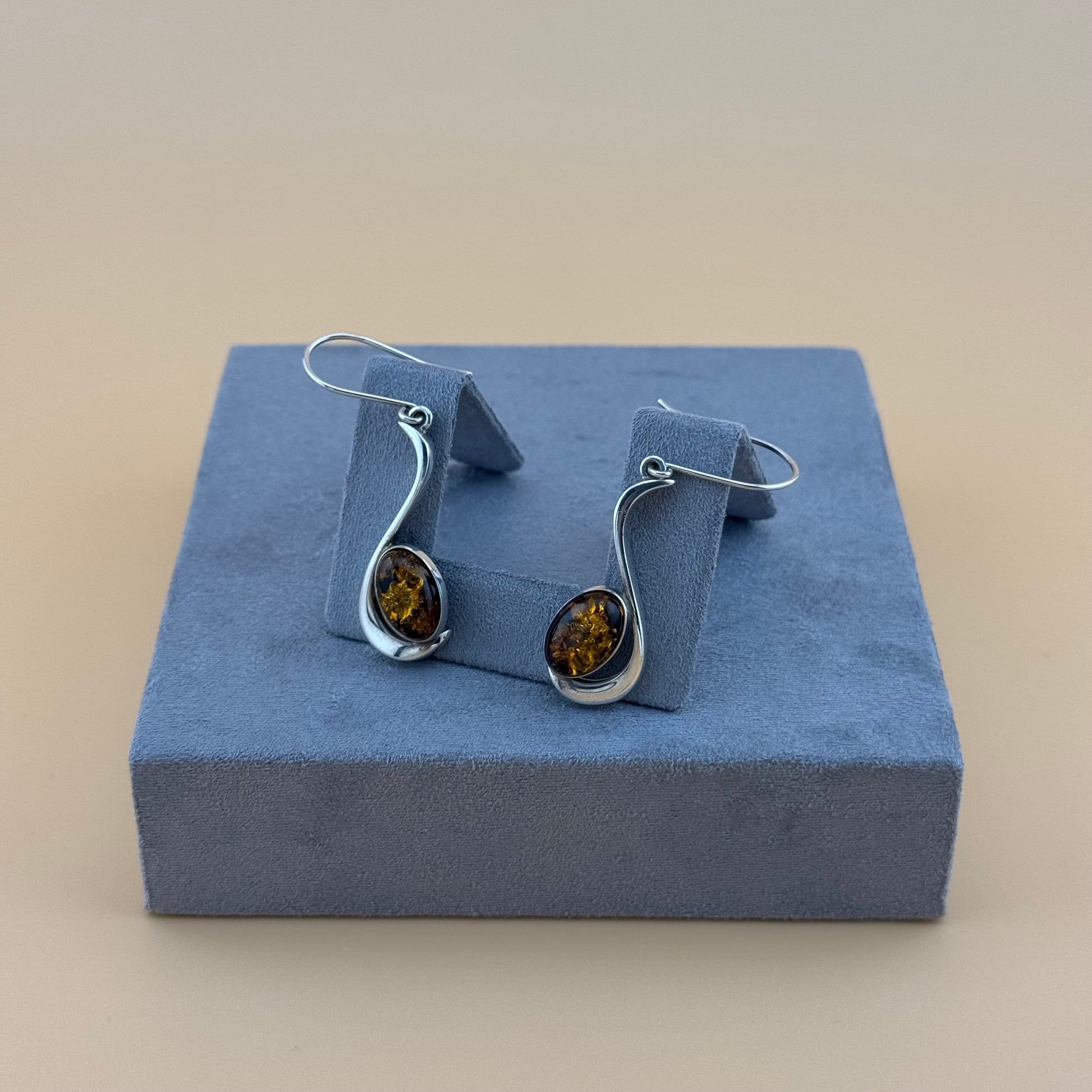 Pair of silver earrings with amber stones on a blue cushioned stand.
