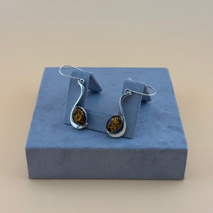 Pair of silver earrings with amber stones on a blue cushioned stand.