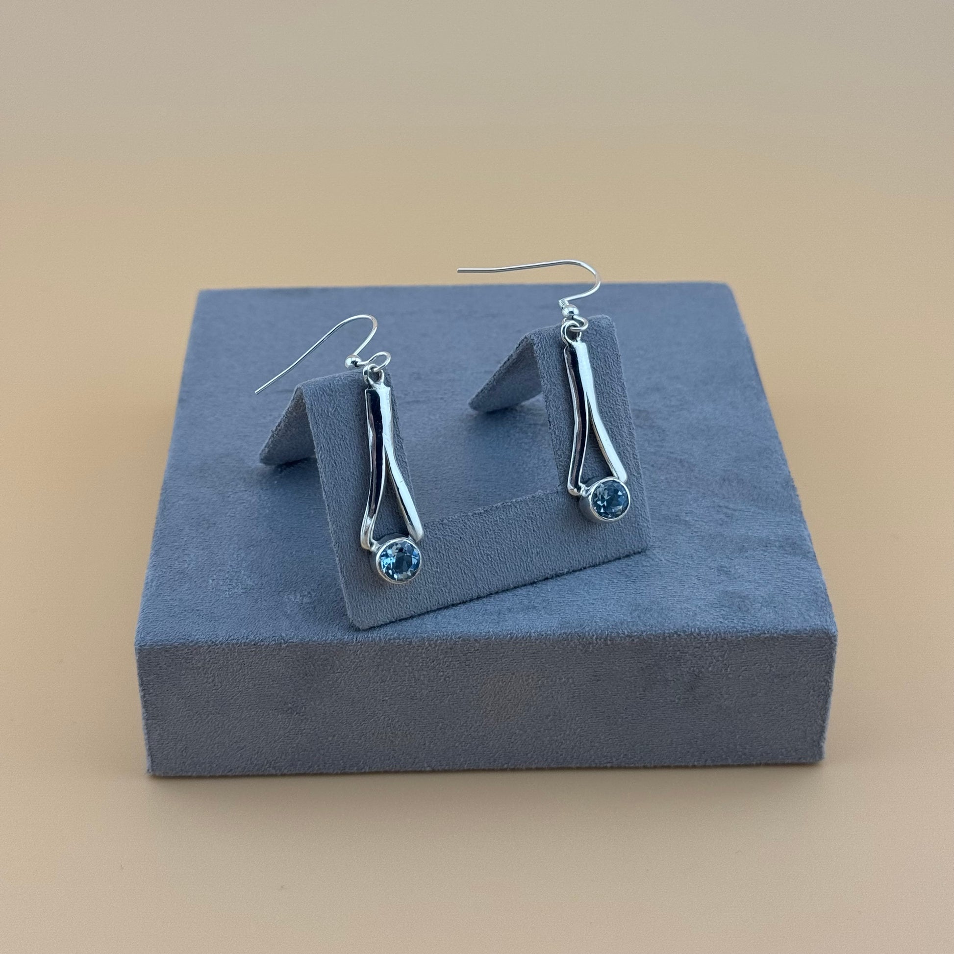 Silver earrings with blue aquamarine gemstones on a gray jewelry display box against a beige background