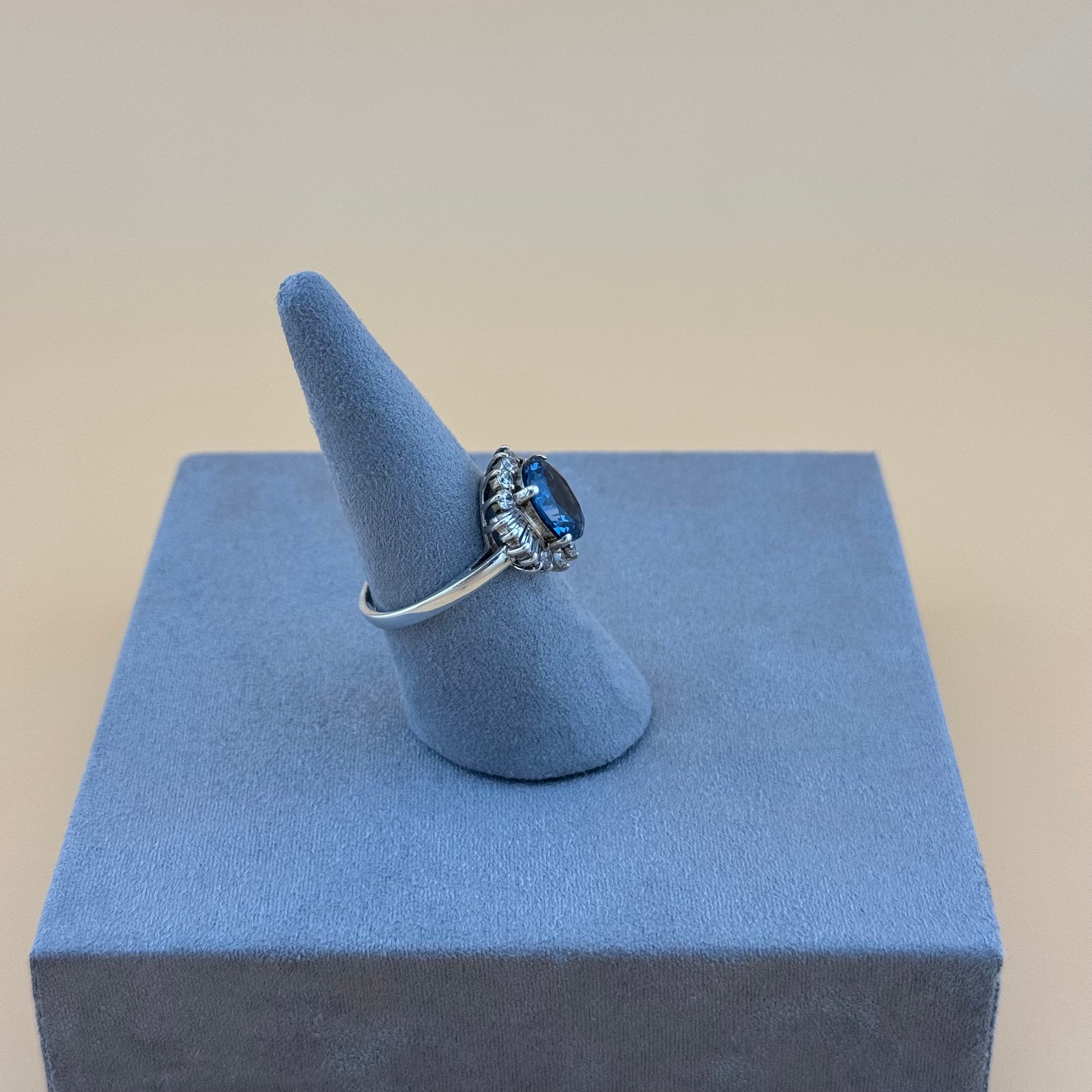 Ring with a blue topaz gemstone on a gray cone-shaped stand against a beige background