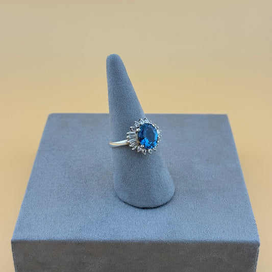 Silver ring with a blue topaz gemstone on a gray stand against a beige background