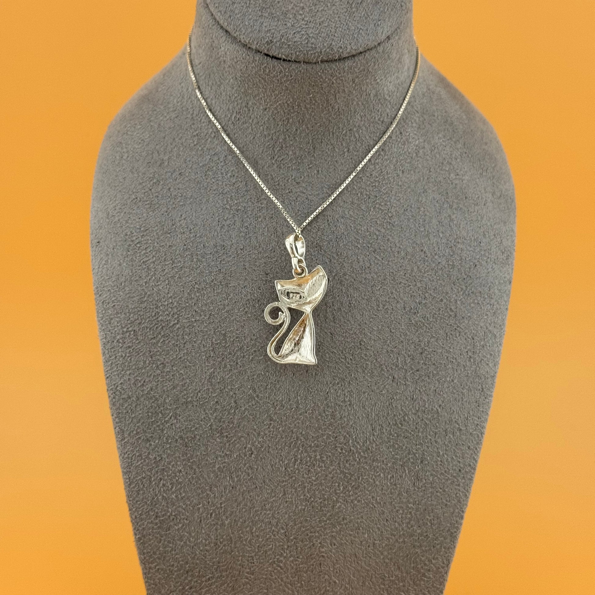 Silver pendant necklace on a gray mannequin bust against an orange background