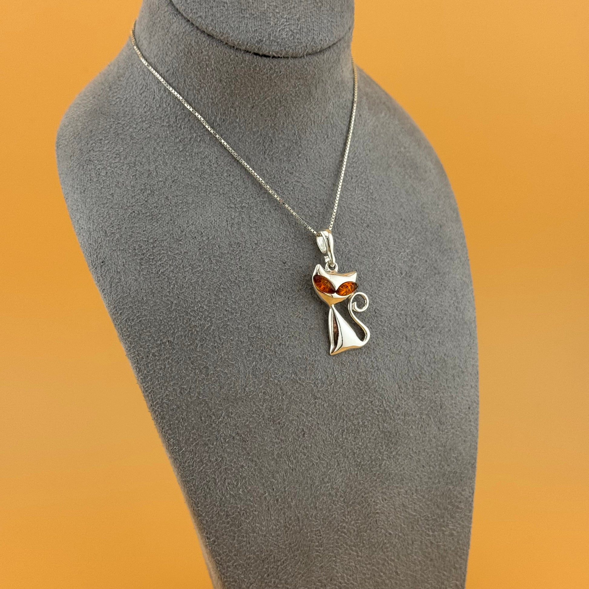 Silver necklace with a cat-shaped pendant on a mannequin bust against an orange background
