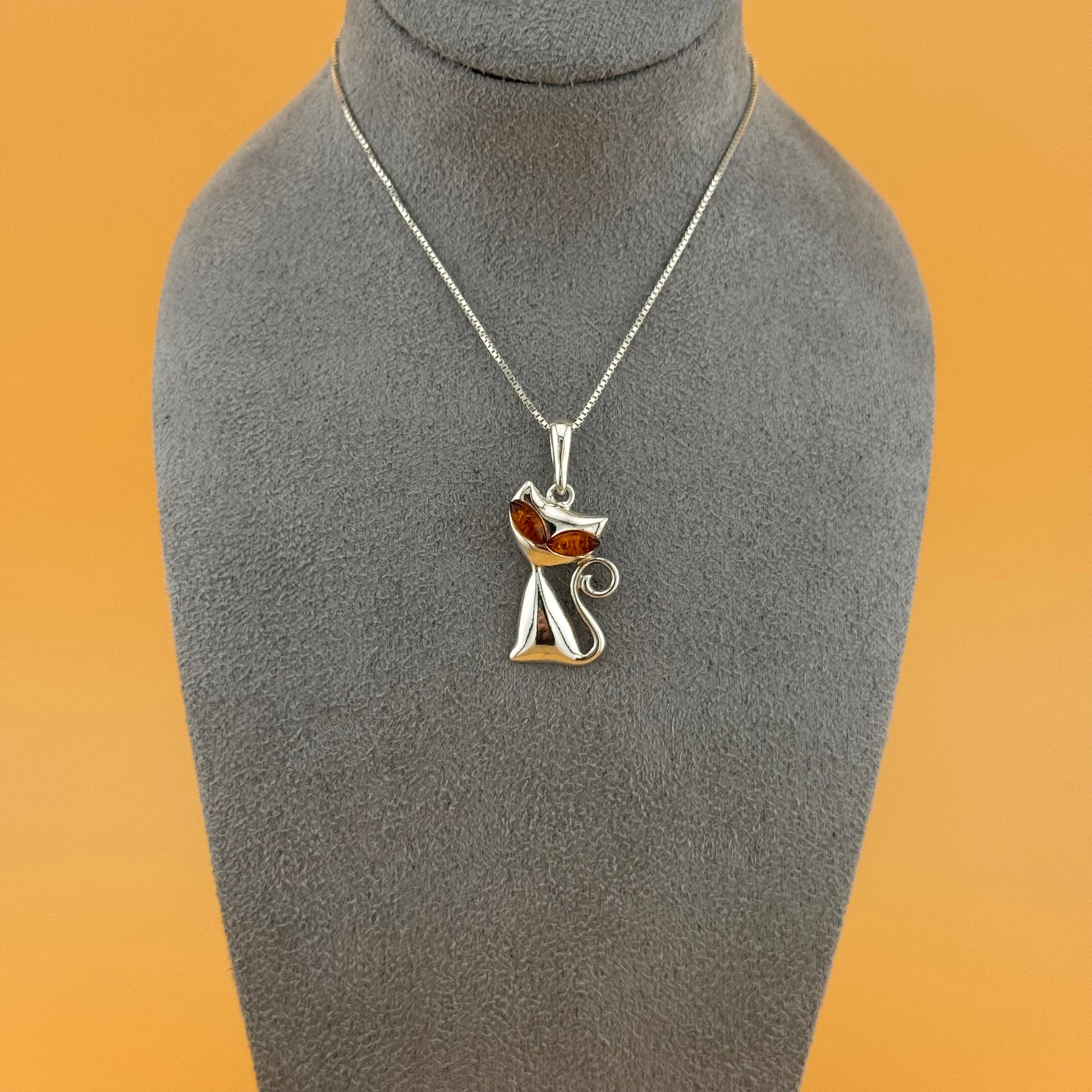 Silver necklace with a cat-shaped pendant on a gray mannequin bust against an orange background