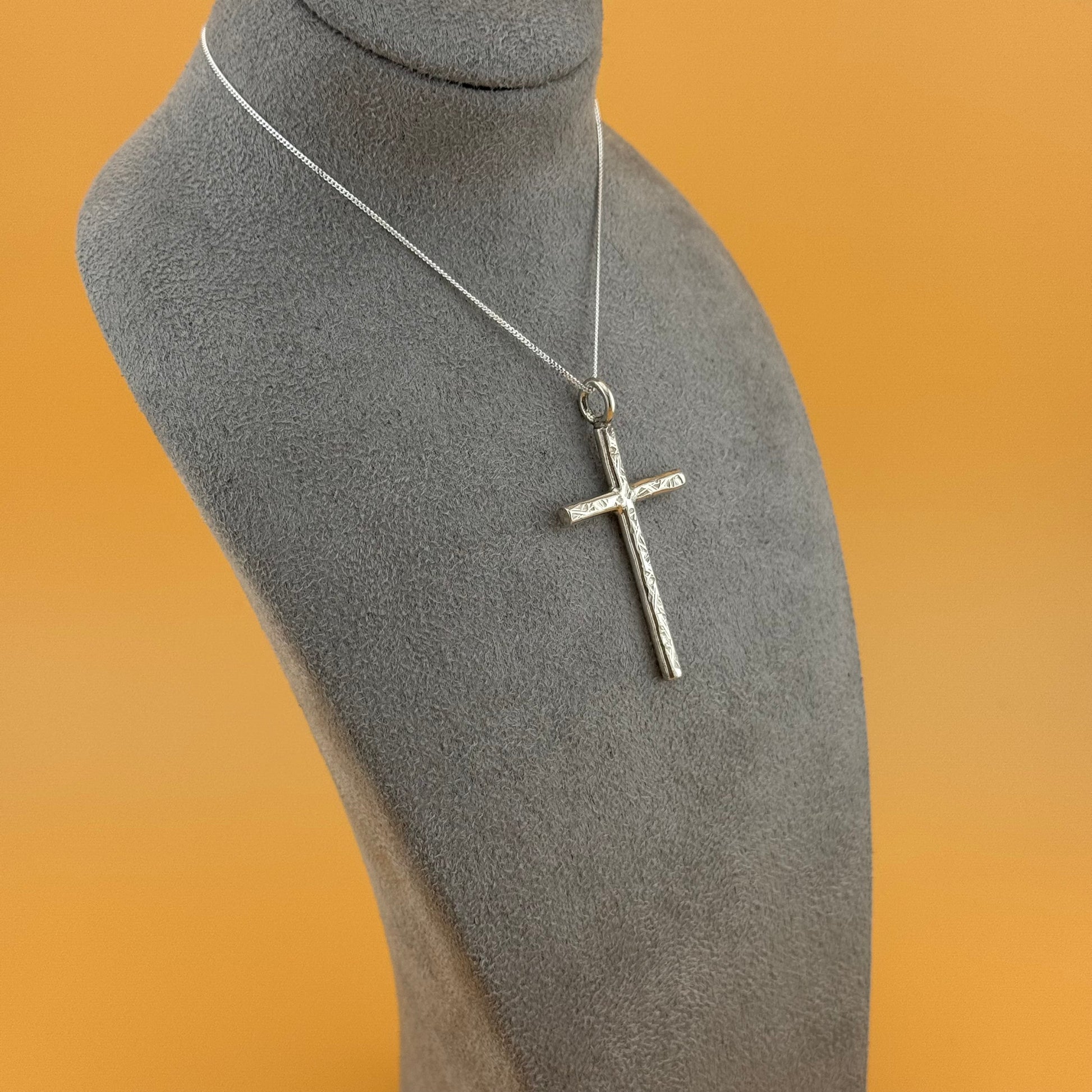 Silver cross necklace on a gray mannequin bust against an orange background