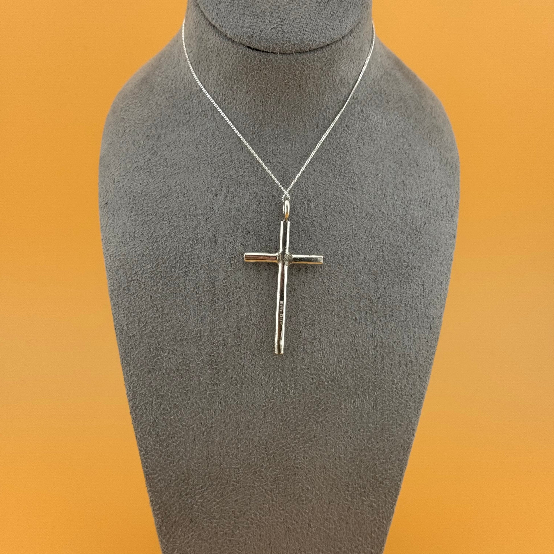 Silver cross pendant on a mannequin bust with an orange background