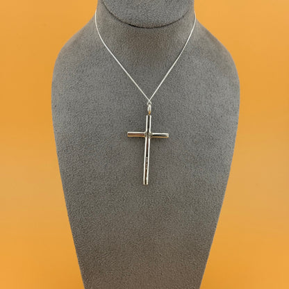 Silver cross pendant on a mannequin bust with an orange background