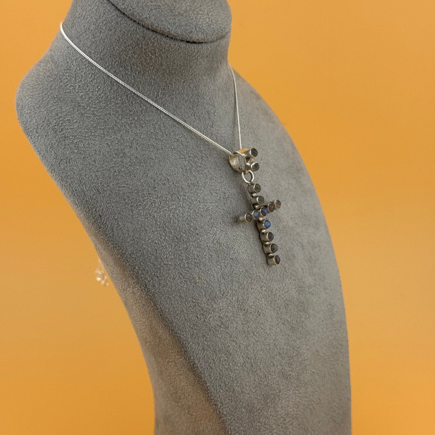 Necklace with a cross pendant on a gray mannequin bust against an orange background